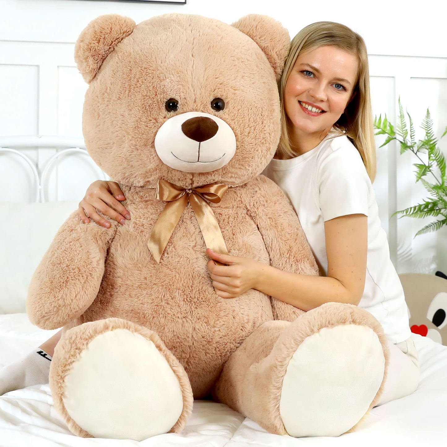 Woman holding a large teddy bear with a bow tie in a bright room.
